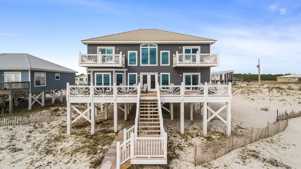 A beachfront house with a two-story deck and a staircase leading to the entrance. - Luxury gulf front home with huge windows facing the Gulf. Large open decks (Gulf Shores)