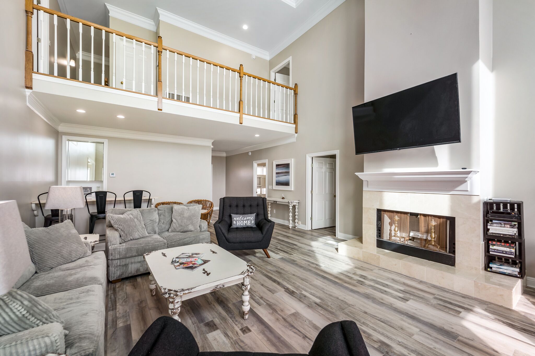 A spacious living room with a high ceiling, a fireplace, a flat-screen TV, and a staircase leading to an upper level.