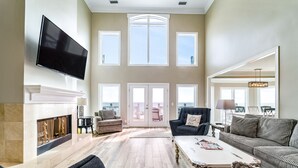 A spacious living room with a fireplace, a large TV, and a view of the outdoors through the windows. - Luxury gulf front home with huge windows facing the Gulf. Large open decks (Gulf Shores)