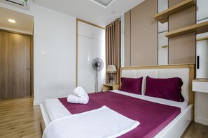 A modern hotel room with a large bed, a wooden wardrobe, a bedside table with a lamp, and a fan. - Christina's Saigon - Icon 56 Apartment (Ho Chi Minh City)