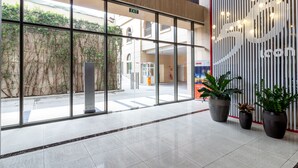 Entrada de um edifício moderno com portas de vidro, plantas em vasos e sinal de saída.
