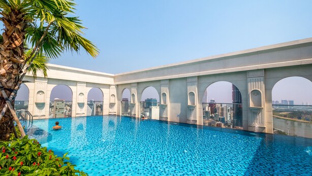 Piscina com vista para a cidade, cercada por arcos e palmeiras.