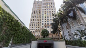 Um edifício alto e moderno, com fachada simétrica, rodeado por vegetação e palmeiras.