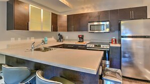 A modern kitchen with dark cabinets, stainless steel appliances, a central island with bar stools, and a built-in microwave. - Charming Historic Condo (Asheville)