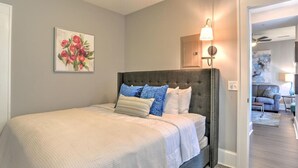 A bedroom with a bed, a headboard, a wall-mounted lamp, and a painting. - Charming Historic Condo (Asheville)