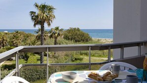 A balcony with a table set for breakfast, overlooking a beach and palm trees. - Les Capitelles by Interhome (Saint Cyprien)