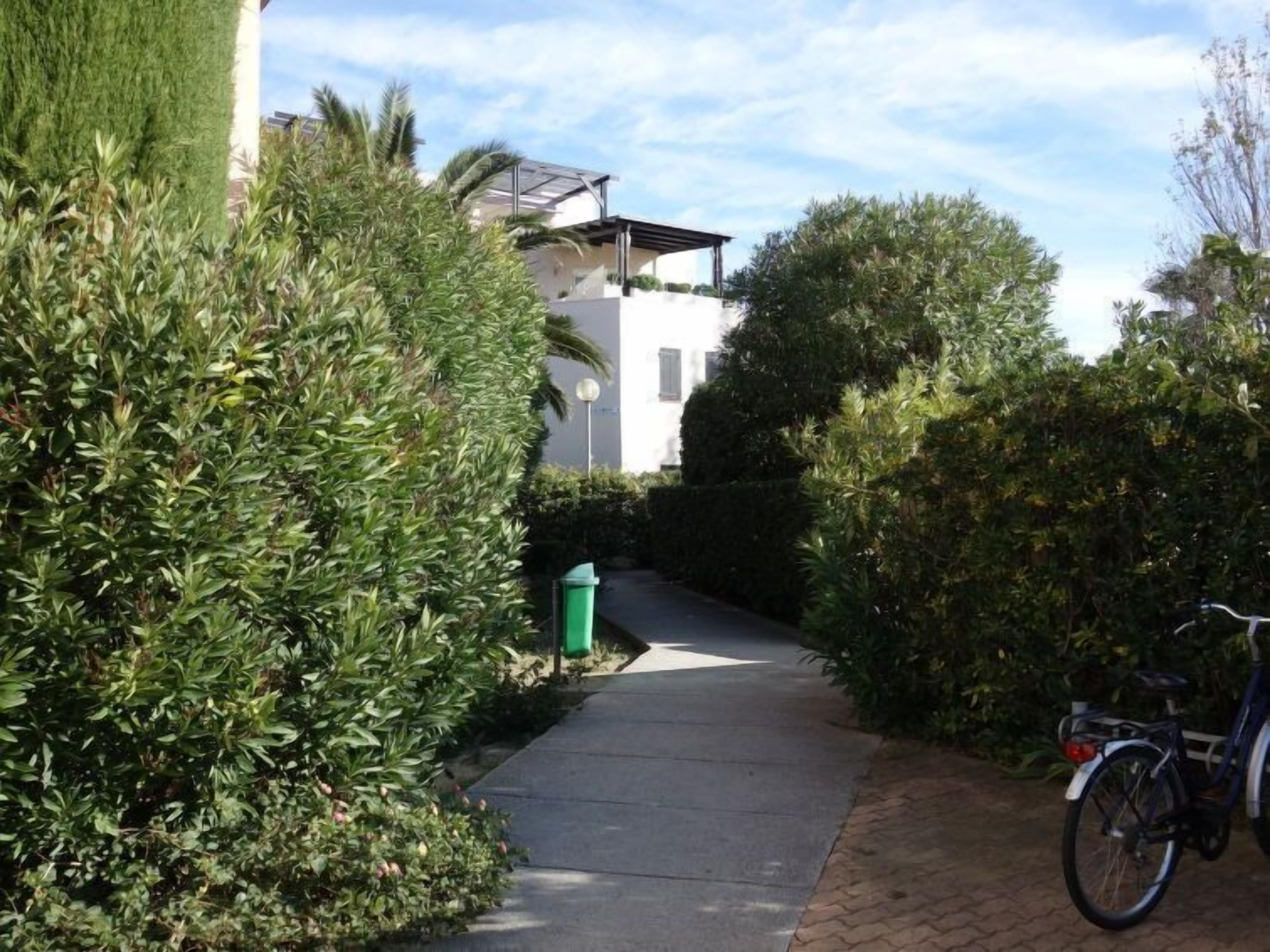 Um caminho estreito ladeado por sebes verdes densas e uma bicicleta estacionada à direita.
