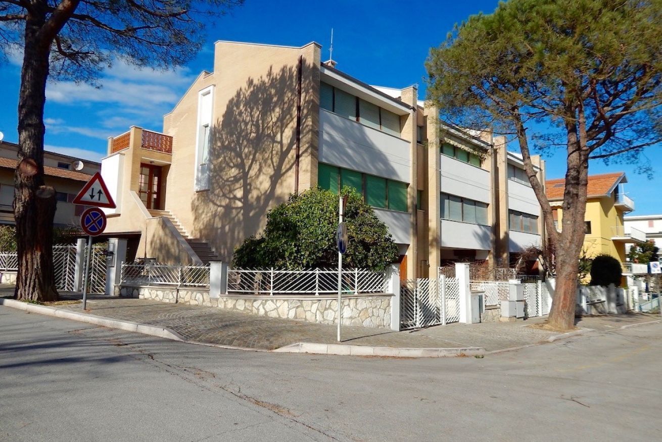 Un edificio moderno con tetto piatto, una scalinata che conduce all'ingresso e un recinto bianco che circonda la proprietà.