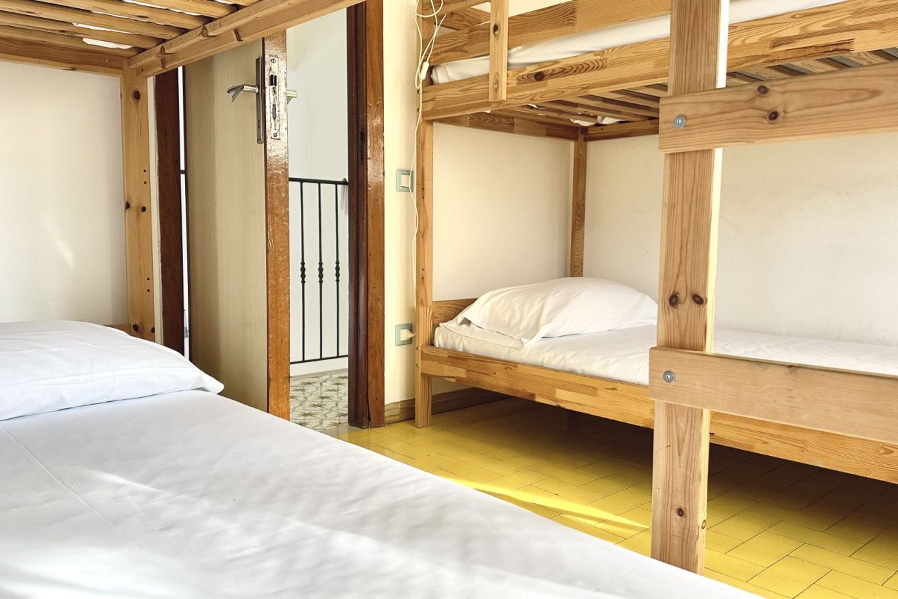 Una habitación con dos literas, vigas de madera, una puerta y suelo amarillo.
