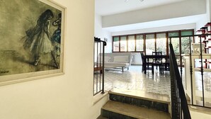 Een trap leidt naar een kamer met een bed, een eettafel en stoelen. Boven de trap hangt een plafondventilator.