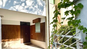 Een modern gebouw met een houten gevel, een duidelijke deur en een witte omheining begroeid met klimplanten.
