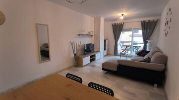 Een moderne woonkamer met een bank, televisie en eethoek.