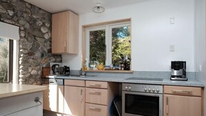 Uma cozinha moderna com parede de pedra, armários de madeira, forno embutido e janela com vista para o verde.