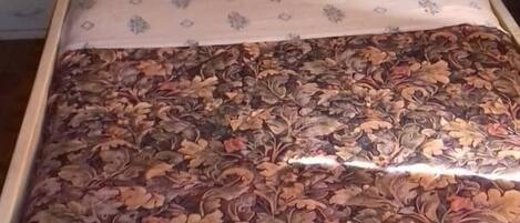 A bed with a floral bedspread, a white headboard, and a small bedside table.