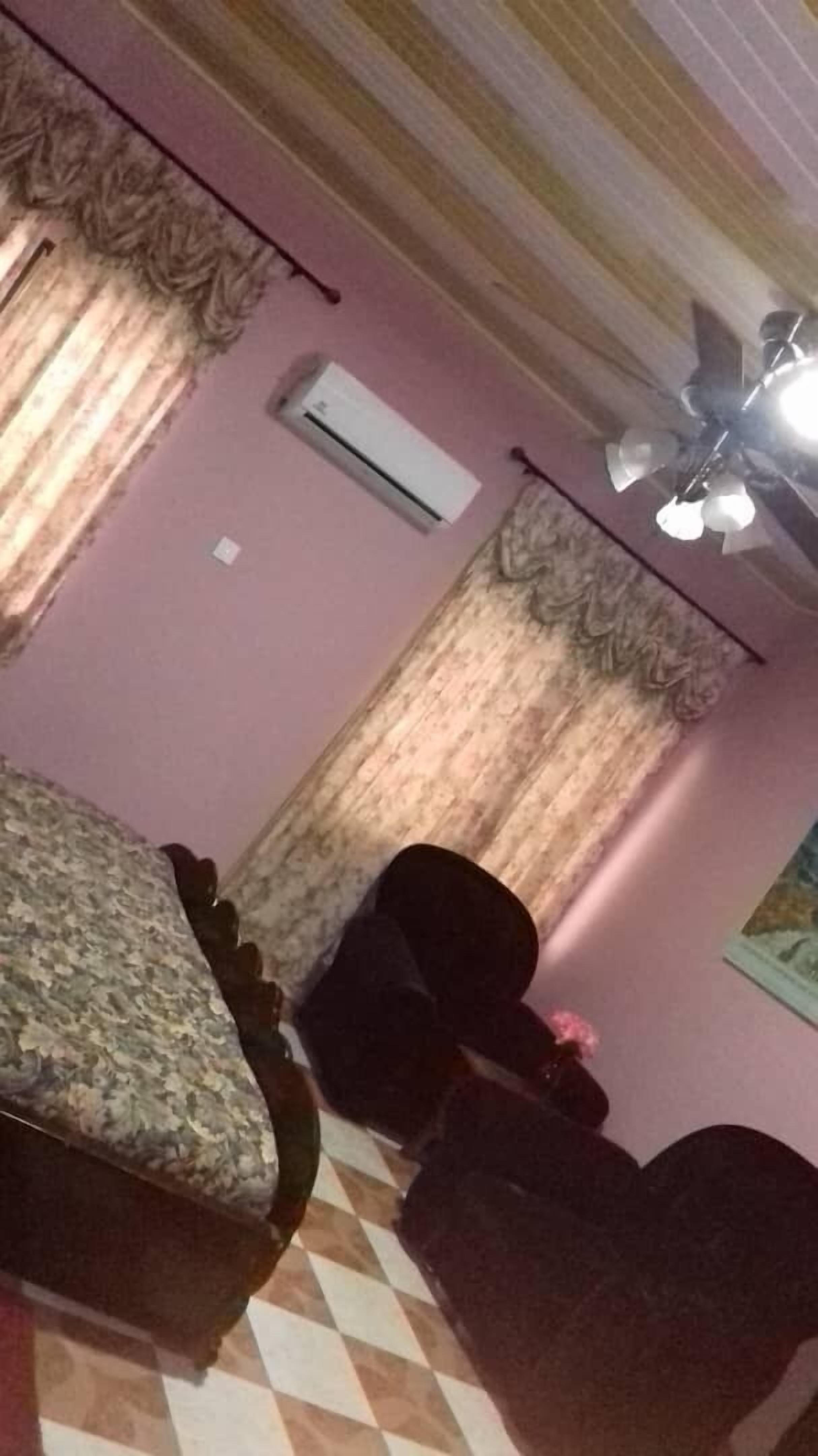 A room with a bed, two chairs, a ceiling fan, and an air conditioning unit.