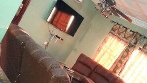 Un salon avec un canapé en cuir marron, un climatiseur, un ventilateur de plafond et des carreaux de sol à motifs.