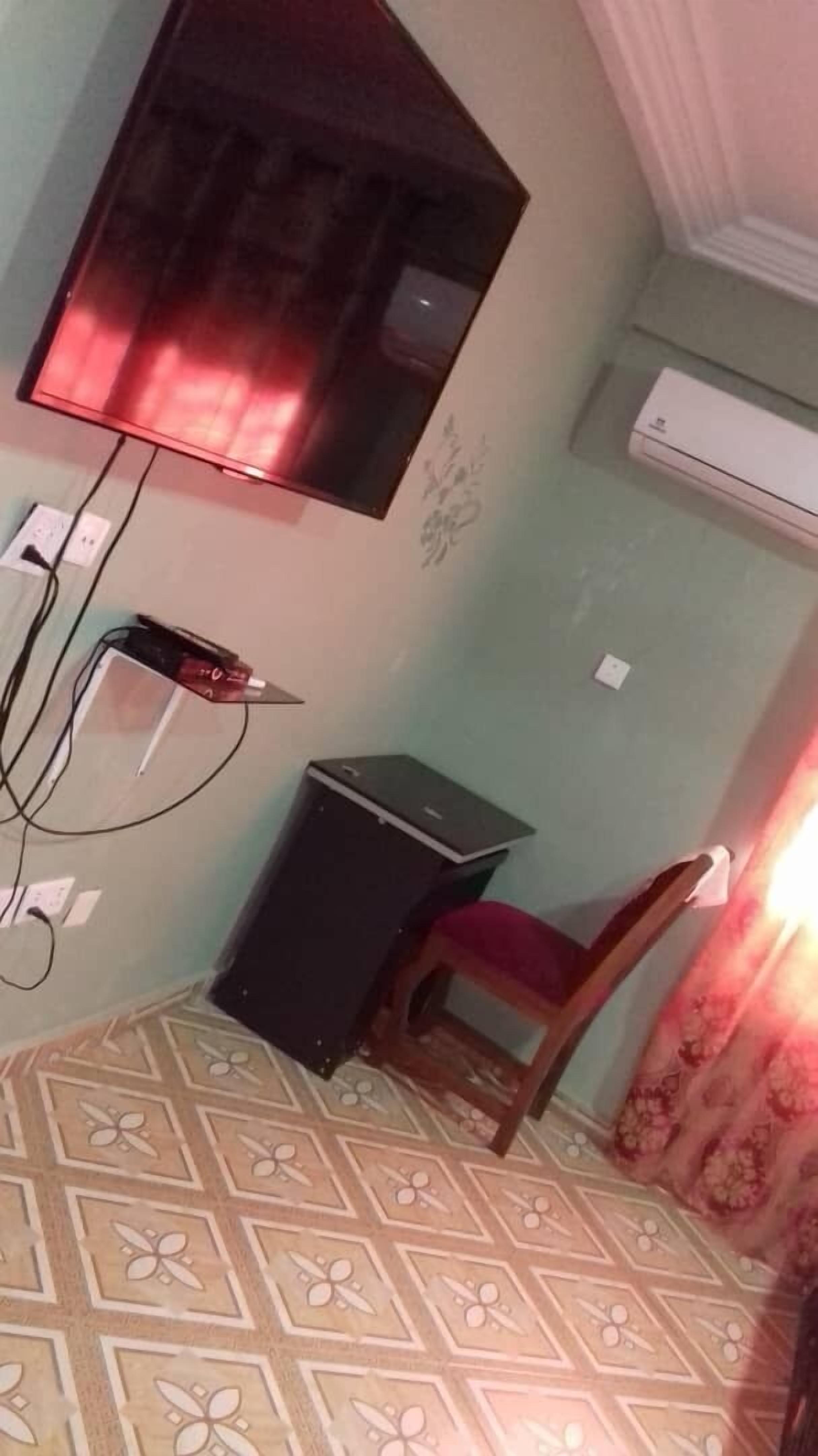 Una habitación con una cama, un escritorio, una silla, un televisor montado en la pared y un equipo de aire acondicionado.