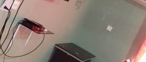 Una habitación con una cama, un escritorio, una silla, un televisor montado en la pared y un equipo de aire acondicionado.