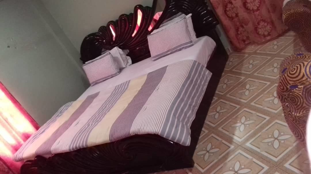 A neatly made bed with striped bedding, a dark wooden headboard, and a patterned floor.