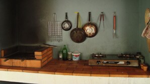 Une cuisine équipée d’un four à briques, d’une cuisinière à gaz et de divers ustensiles de cuisine accrochés au mur.