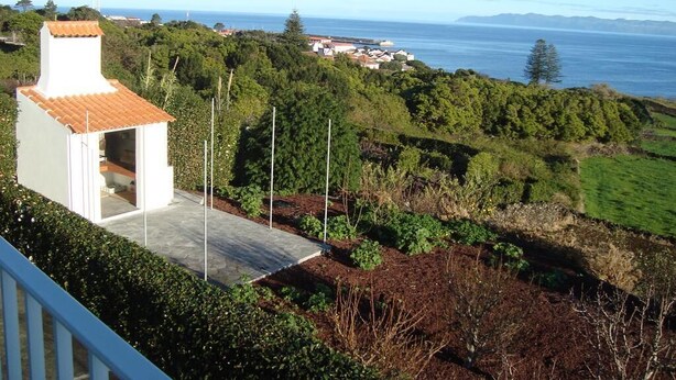 Une propriété située sur la côte, avec un bâtiment blanc doté d’un toit en tuiles, d’une terrasse pavée et offrant une vue sur la mer et les collines lointaines.