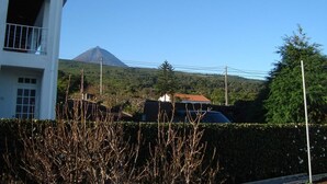 Un bâtiment doté d’un balcon, avec une montagne en arrière-plan et une haie au premier plan.