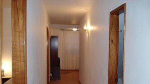 Un couloir étroit, avec des portes en bois de chaque côté, un sol carrelé et un luminaire fixé au mur.