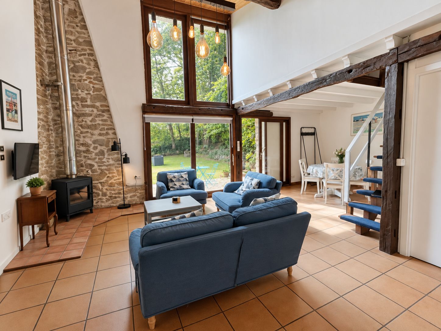 Amplia sala de estar con pared de piedra, chimenea, sofá y escalera que conduce a otro nivel.