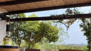 A wooden table with a bottle, a bowl, plates, and a basket of vegetables under a bamboo roof.