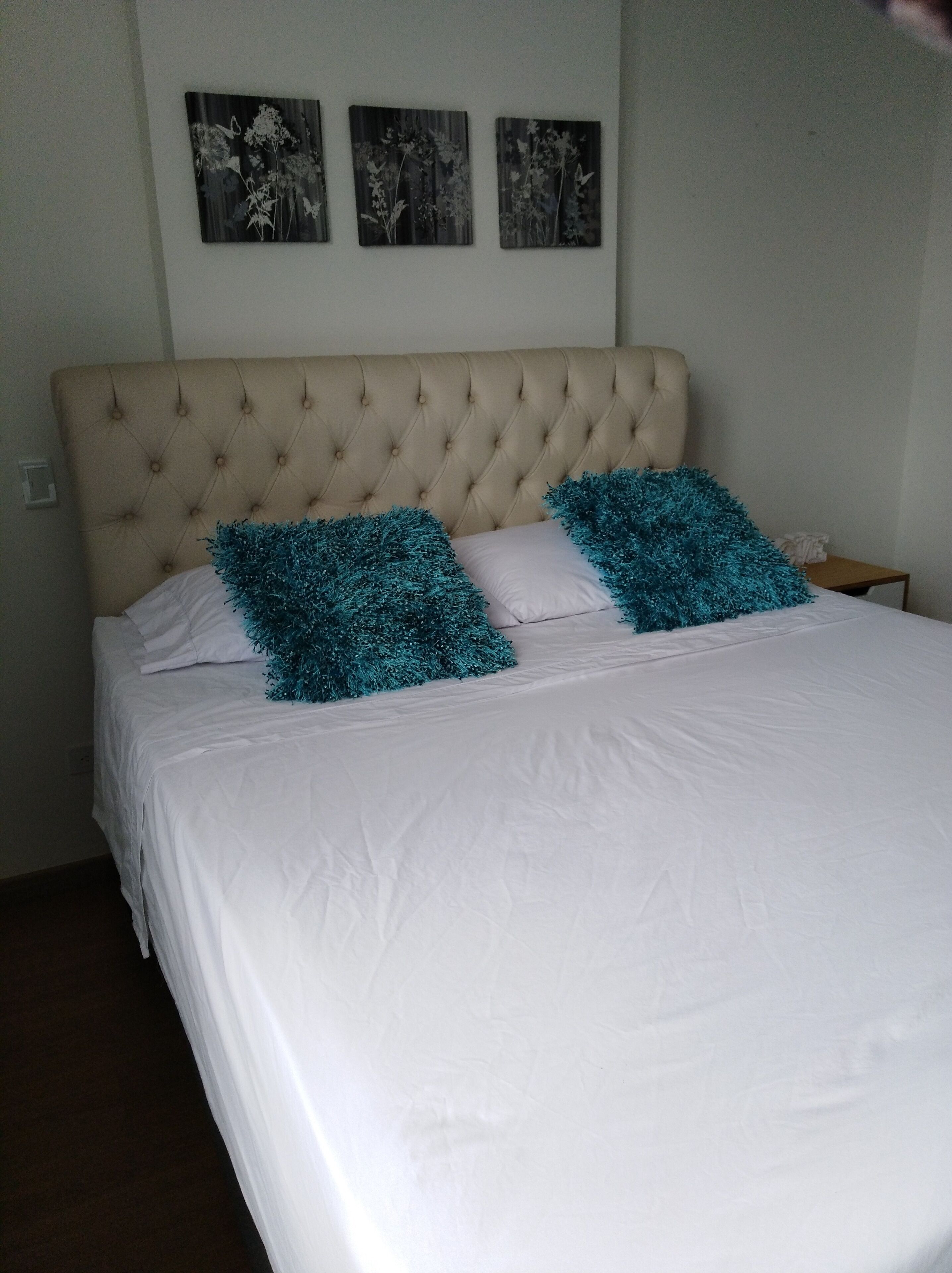 Uma cama com cabeceira estofada, roupa de cama branca e duas almofadas decorativas verde-água.