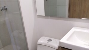 A modern bathroom with a white toilet, a wooden cabinet, and a glass shower enclosure. - Gran apartamento en plaza principal (Guatape)