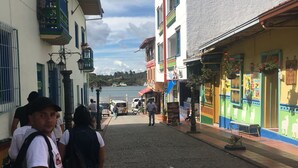 A cobblestone street with buildings on either side, a clear sky, and a body of water in the distance. - Gran apartamento en plaza principal (Guatape)