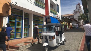 A street scene with a white building featuring balconies with green railings and a blue awning. - Gran apartamento en plaza principal (Guatape)