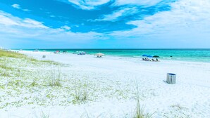 Een strand met wit zand, helder turquoise water en enkele strandparasols.