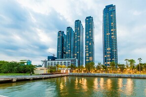 Une vue sur le front de mer, avec de hauts immeubles, un parc arboré et une étendue d’eau calme dans laquelle se reflètent les bâtiments.