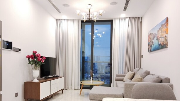 Ein modernes Hotelzimmer mit einem großen Bett, einer Sitzecke, einem Fernseher, einem kleinen Tisch und einem Balkon mit Blick auf die Stadt.