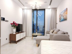 Una habitación de hotel moderna con una cama grande, un sofá, un televisor, una mesita y un balcón con vista a la ciudad.