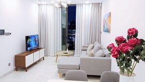 Ein modernes Wohnzimmer mit einer Couch, einem Couchtisch und einem Fernseher. Es gibt ein großes Fenster mit Vorhängen, eine Topfpflanze und ein Gemälde an der Wand.