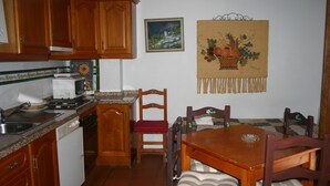 Una cocina con armarios de madera, microondas, lavabo y una mesa de comedor con sillas.