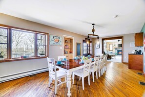 A dining area with a wooden table, white chairs, and a view through large windows.