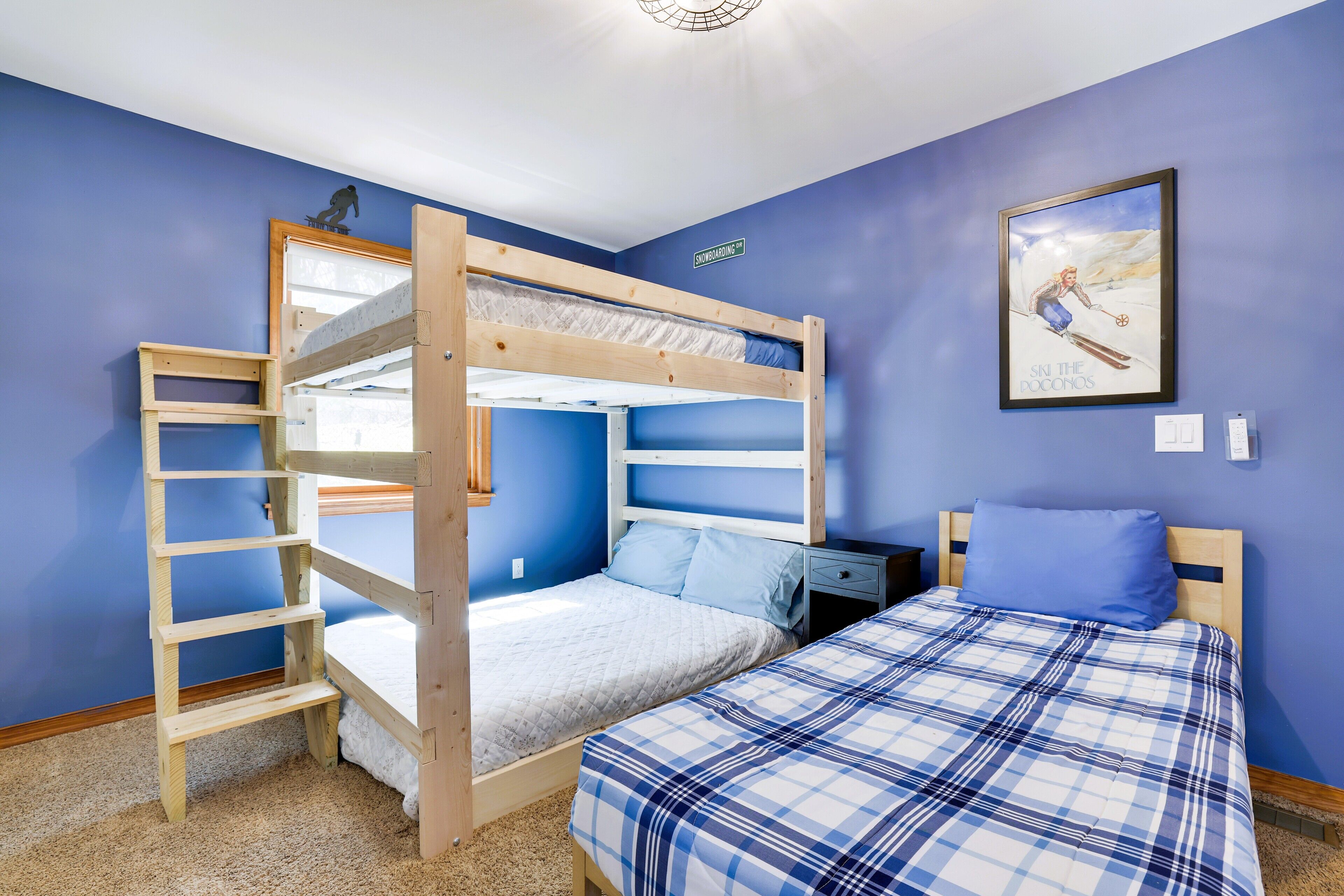 A bunk bed room with a ladder, a desk, and a framed picture on the wall.