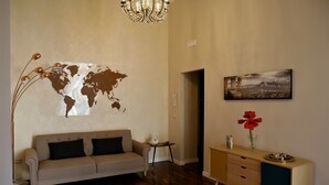 A living room with a world map on the wall, a sofa, a small table with a swan figurine, a cabinet with a vase of red flowers, and a chandelier. - B&B Binario 39 (Naples)