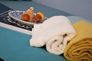 Une salle de bain bien rangée, avec une serviette bleue, une serviette jaune et une assiette décorative ornée d’une figurine et d’une bougie.