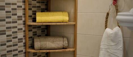 A bathroom with a toilet, a shelf with towels, a hairdryer, and a tiled wall.