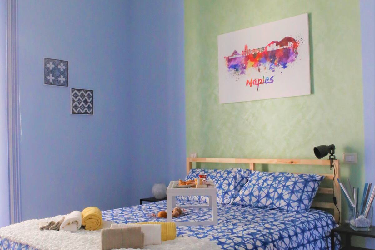 Ein Schlafzimmer mit einem Bett, einem Nachttisch, einer Lampe und einem Wandbild.