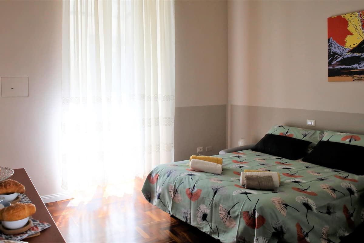 Ein Schlafzimmer mit einem Bett, einem Tisch mit Frühstücksgebäck und einem Fenster mit Vorhängen.