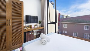 Een hotelkamer met een groot bed, een houten garderobe, een televisie en uitzicht op gebouwen door een groot raam.