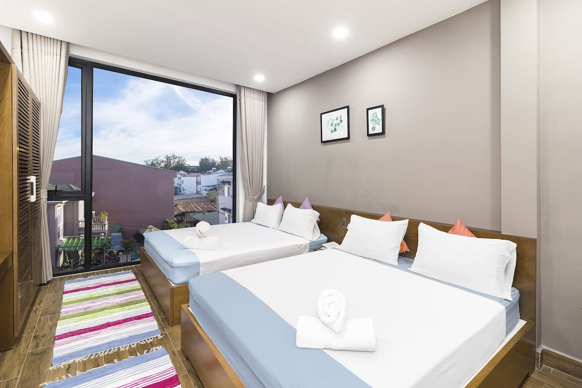 A hotel room with two beds, a large window, and a view of buildings outside.