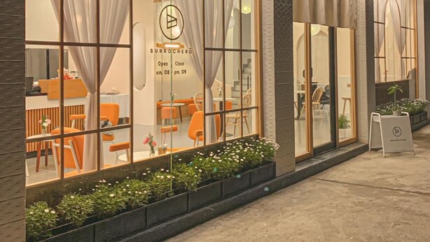 Een modern gebouw met grote ramen, een zichtbaar restaurantinterieur en een bord waarop de openingstijden staan.