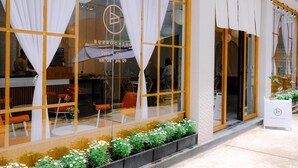 Een restaurant met grote ramen, witte gordijnen en een terras.